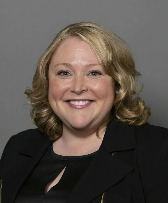 Headshot of Jessica August smiling wearing a black top and zippered black blazer