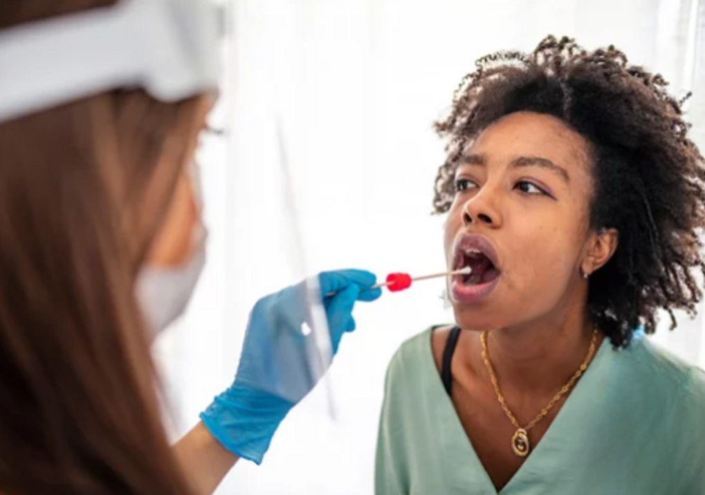 Hygienist holding swab for saliva testing with open-mouthed patient