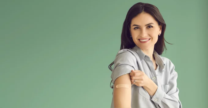 Woman holding right sleeve up with left had to show an upper arm bandaid