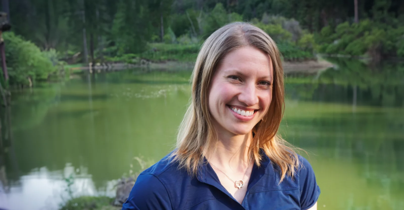 Kristin Maxwell standing at a peaceful pond surrounded by forest