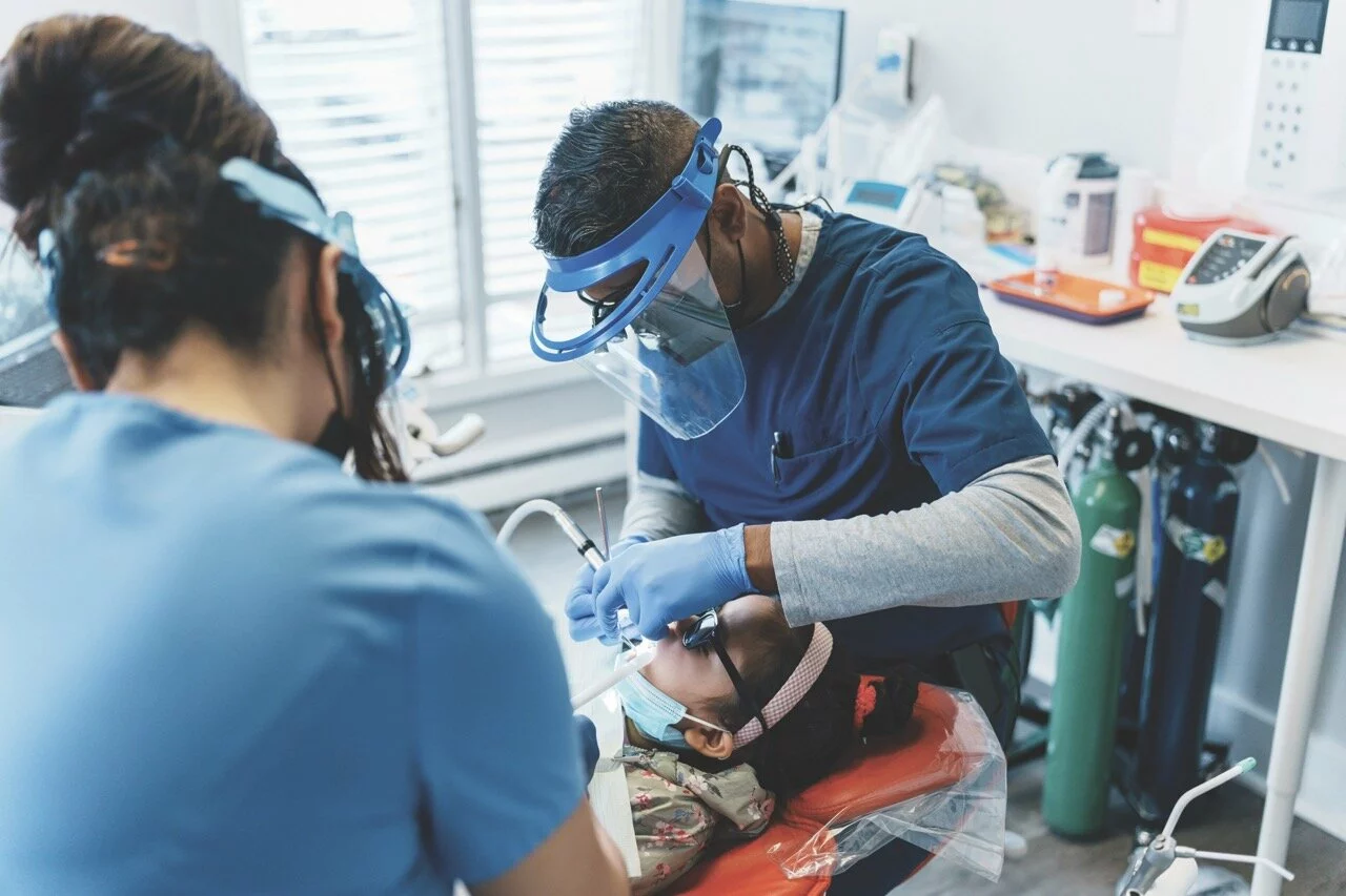 Indian, male dentist and his female dental assistant performs a procedure on a young girl of Asian descent. 2025/02/iStock-1554903296-Large.jpeg 