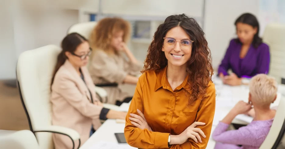 Woman standing in conference room smiling at table with colleagues seated